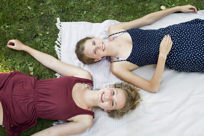 Overhead portrait of two teenage girls lying on picnic blanket in park — Stock Photo
