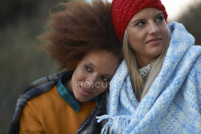 Portrait of two young women huddled in blanket on beach at dusk — Stock Photo