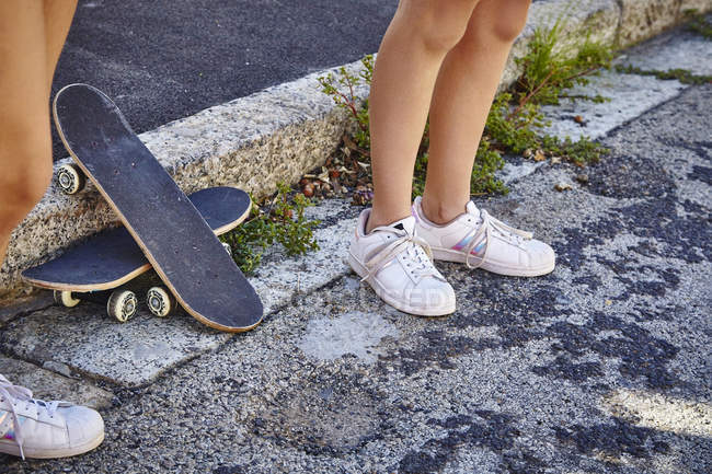 Две подруги, стоящие на улице, скейтборды на полу рядом с ними, низкая секция — стоковое фото