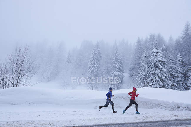 Side view of man and woman jogging in snow covered forest, Gstaad, Switzerland — Stock Photo