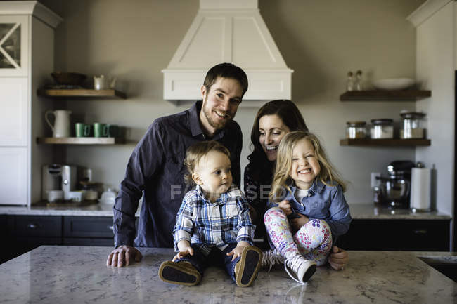 Portrait of mid adult parents with girl and baby boy on kitchen counter — Stock Photo