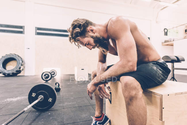 Entraîneur masculin épuisé prenant une pause de l'haltérophilie dans la salle de gym — Photo de stock