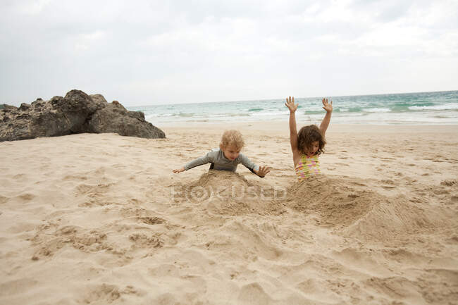 Boy and girl buried in sand on beach — Stock Photo