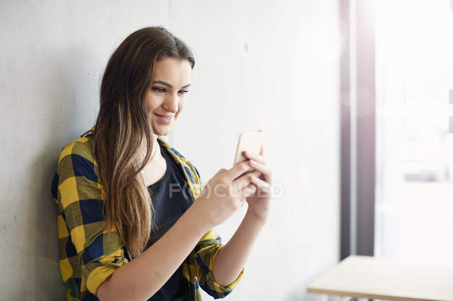 Giovane studentessa che legge il testo dello smartphone al college di istruzione superiore — Foto stock