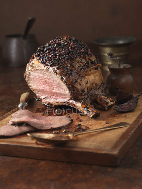 Lomo de cerdo con corteza de pimienta y glaseado en rodajas sobre tabla de madera - foto de stock