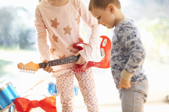 Дівчина і брат грають з іграшковою гітарою в різдвяний день — стокове фото