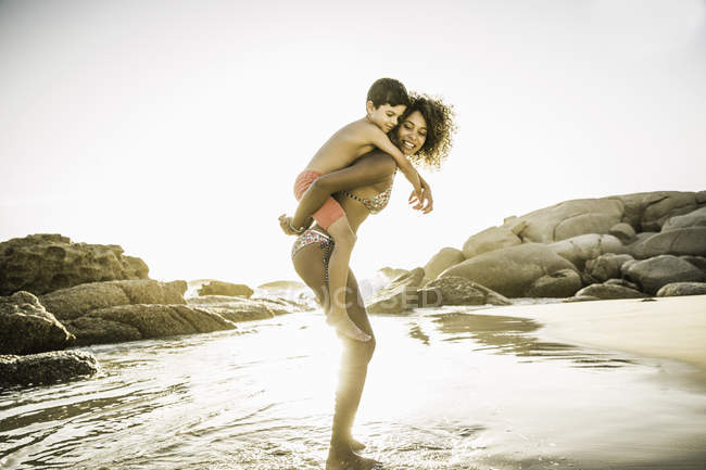 Mother giving son piggyback ride on beach — Stock Photo