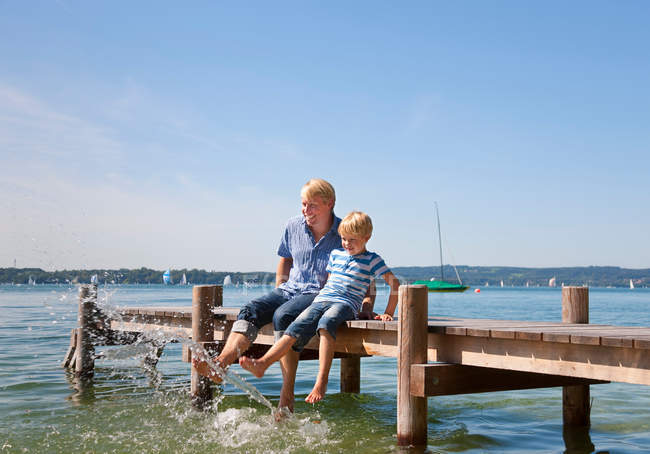 Father and son dangling feet in lake — Stock Photo