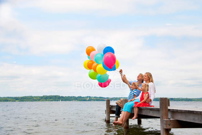 Family holding balloons on wooden pier — Stock Photo