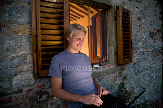Uomo con computer portatile fuori finestra illuminata — Foto stock