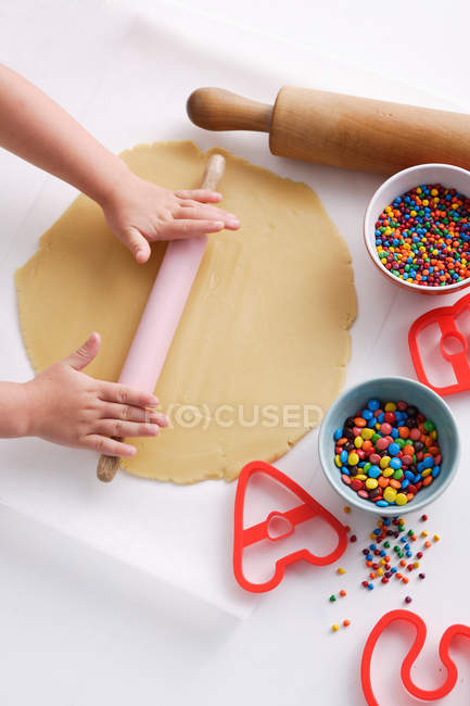 Abgeschnittenes Bild eines Kindes, das Teig mit Nudelholz auf dem Tisch rollt — Stockfoto
