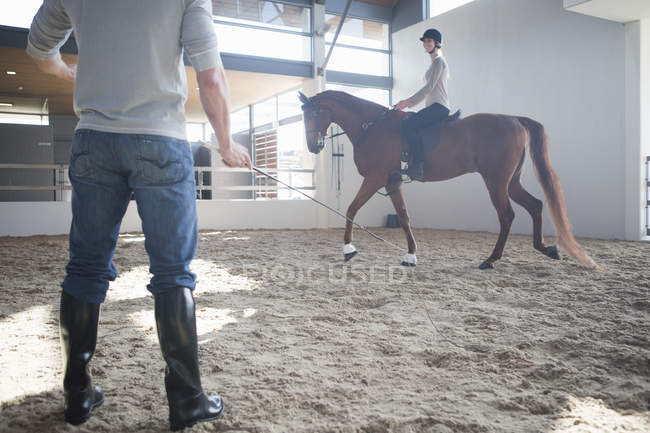 Equitazione femminile con istruttore in paddock al coperto — Foto stock