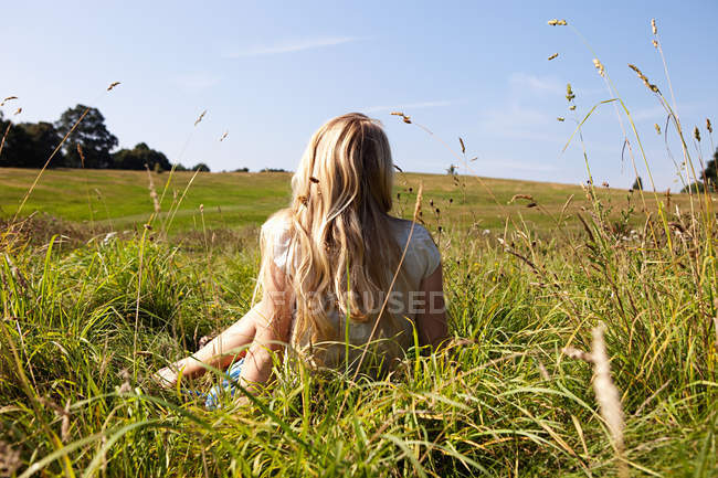 Mujer joven sentada en un campo con espalda a la cámara - foto de stock