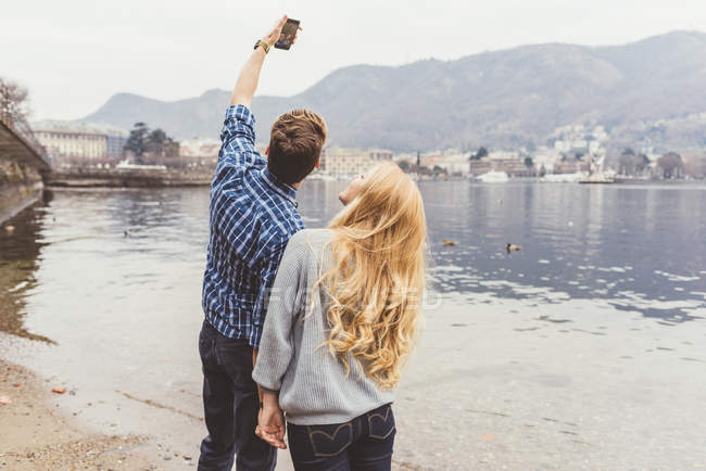 Pareja joven tomando selfie smartphone en la orilla del lago, Lago de Como, Italia - foto de stock
