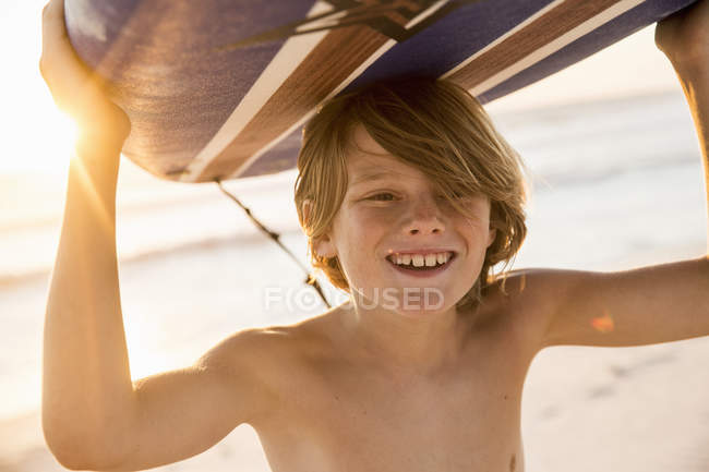 Menino carregando prancha sobre a cabeça sorrindo — Fotografia de Stock