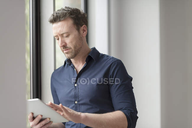 Homem usando tablet digital pela janela do escritório — Fotografia de Stock