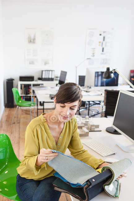 Reife Frau im Büro sitzt am Schreibtisch und schaut durch Stoffmuster — Stockfoto