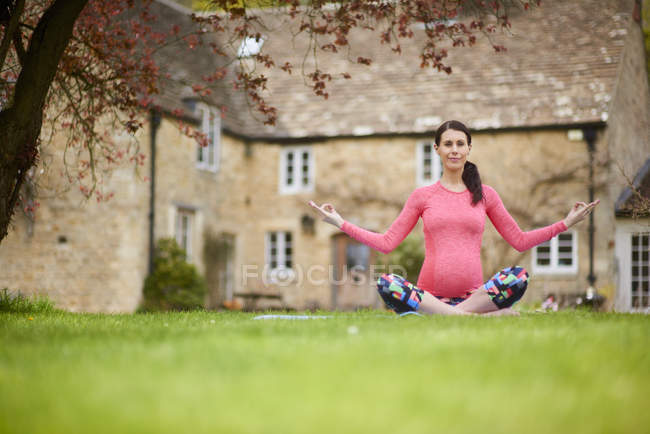 Pregnant woman sitting outdoors, in yoga position — Stock Photo