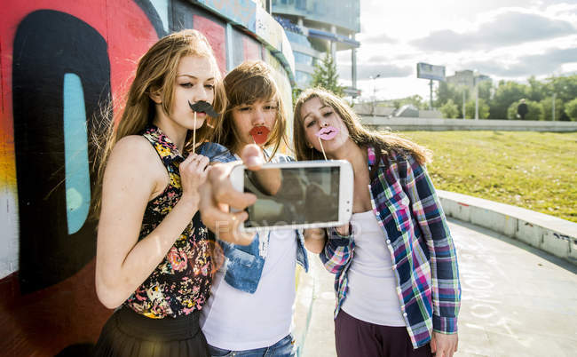 Friends taking selfie wearing fake lips and mustaches in city — Stock Photo