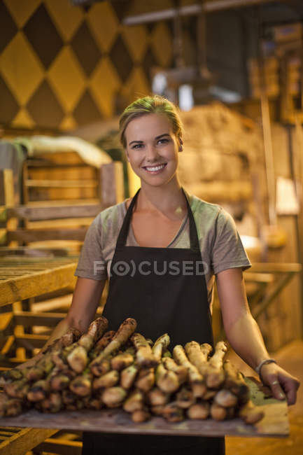 Portrait of young female baker carrying a tray of breadsticks — Stock Photo