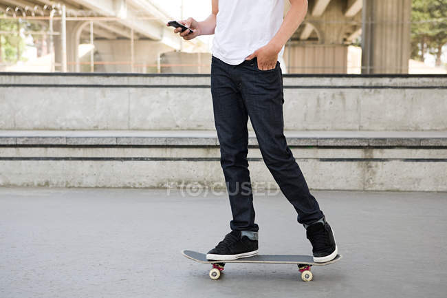 Ragazzo adolescente su skateboard con cellulare — Foto stock