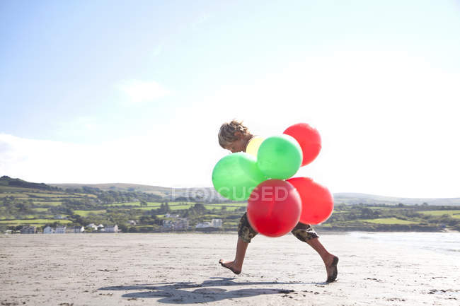 Niño en la playa sosteniendo globos, Gales, Reino Unido - foto de stock