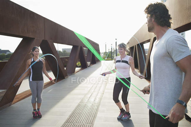 Due donne che saltano sul ponte pedonale urbano con personal trainer maschile — Foto stock