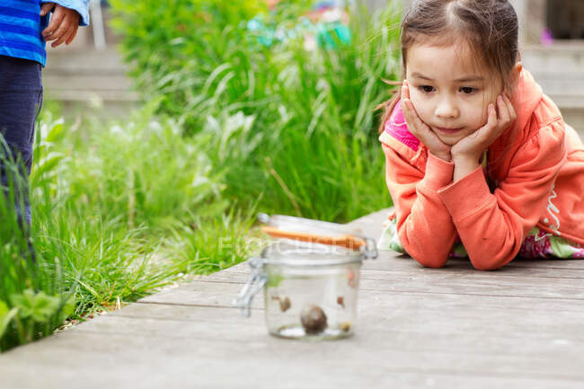 Jeune fille dans le jardin regarder pot d'escargots — Photo de stock