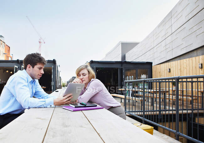 Два человека сидят за столом с цифровым планшетом под открытым небом — стоковое фото