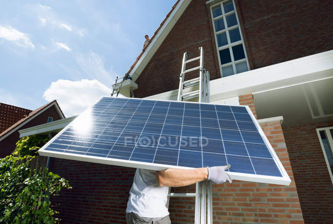 Échelle d'escalade ouvrière portant un panneau solaire pour le toit d'une nouvelle maison, Pays-Bas — Photo de stock