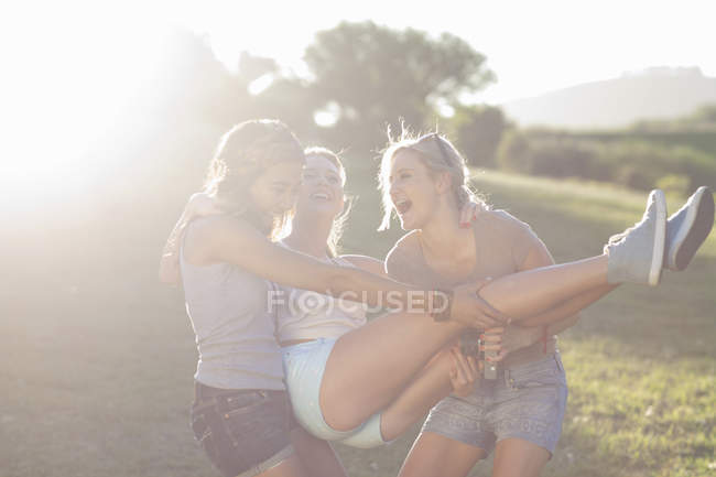 Dos jóvenes hembras tonteando tratando de llevar a su amigo - foto de stock