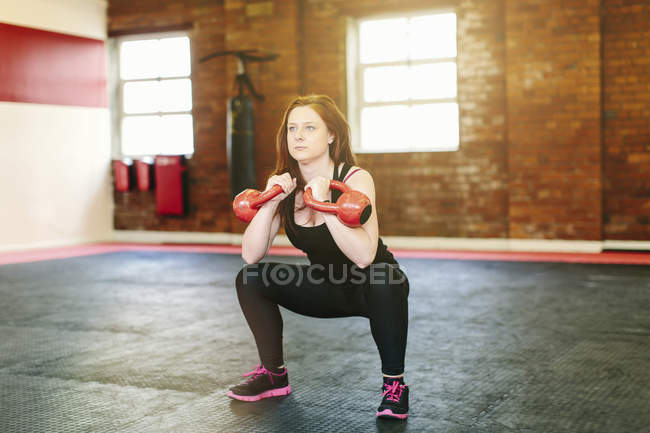 Woman squatting lifting kettlebells — Stock Photo