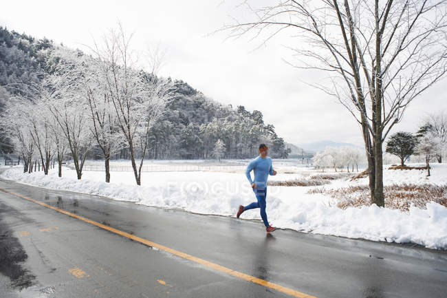 Mature male runner running on road in winter, Lake Kawaguchiko, Mount Fuji, Japan — Stock Photo