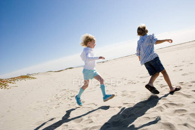 Niño y niña corriendo en la playa - foto de stock