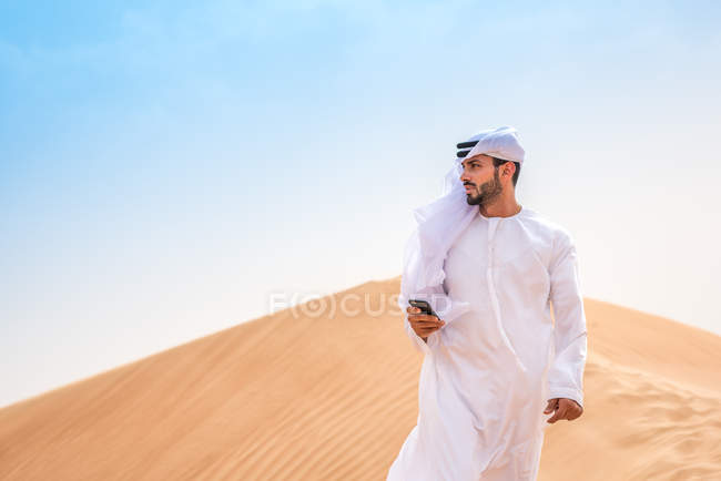 Близькосхідні людині носити традиційний одяг за допомогою смартфона на пустельних дюн, Дубай, Об'єднані Арабські Емірати — стокове фото