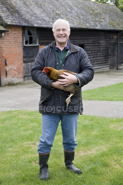 Felice contadino tenendo il pollo all'aperto — Foto stock