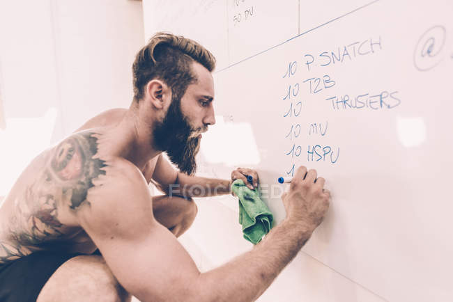 Jeune homme écrivant sur le tableau blanc dans la salle de gym cross training — Photo de stock