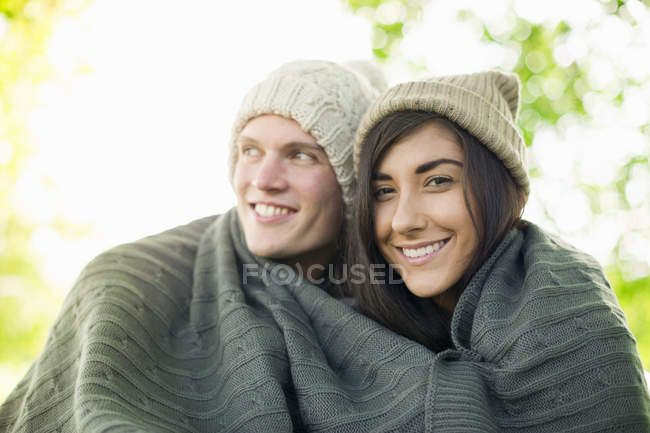 Young couple wearing knit hats wrapped in blanket — Stock Photo