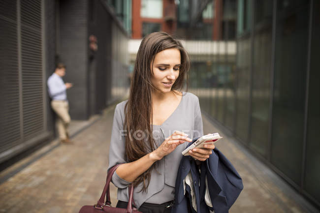 Joven mujer de negocios mensajes de texto en el teléfono inteligente fuera de la oficina, Londres, Reino Unido - foto de stock