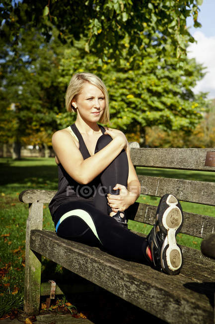 Femme flexion jambe sur banc de parc — Photo de stock