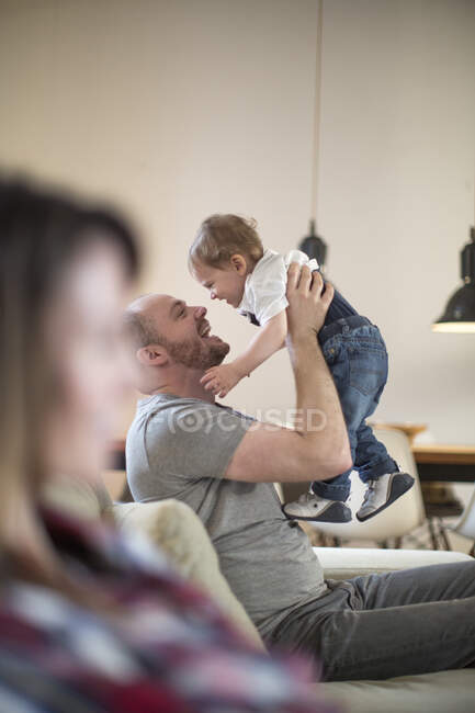 Padre levantando bebé niño cara a cara sonriendo - foto de stock