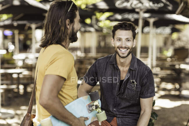 Friends at sidewalk cafe with skateboard — Stock Photo