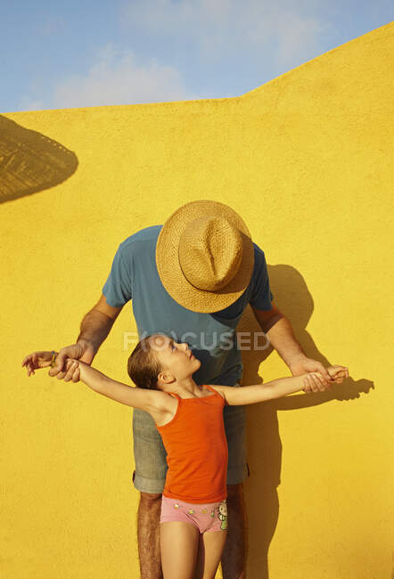 Pai segurando os braços da filha para fora pela parede amarela — Fotografia de Stock