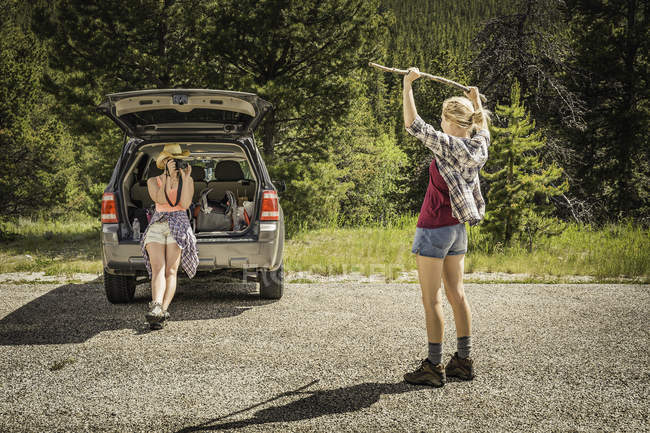 Mujer joven fotografiando senderista adolescente sosteniendo bastón en camino rural, Red Lodge, Montana, EE.UU. - foto de stock