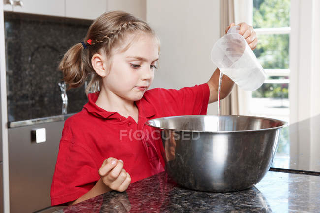 Chica vertiendo agua en el tazón de mezcla - foto de stock