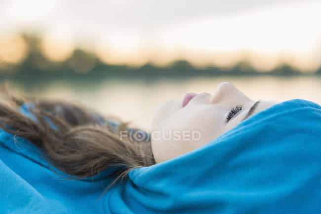 Jovem mulher vestindo top com capuz azul deitado, close-up — Fotografia de Stock