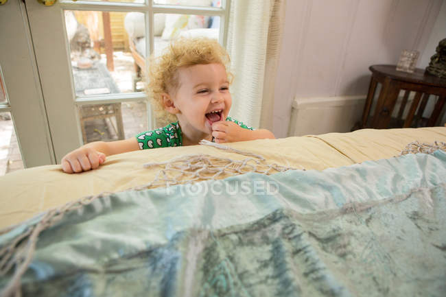 Тоддлер смеется над краем кровати — стоковое фото