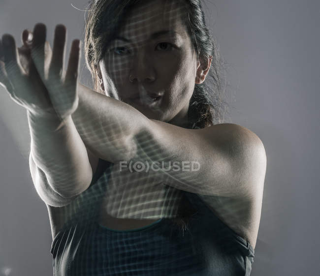 Mitte erwachsene Frau vor grauem Hintergrund, trainierend, Gitter auf Gesicht und Körper projiziert — Stockfoto