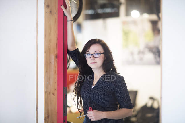 Retrato de mulher encostada à moldura da porta olhando para a câmera — Fotografia de Stock