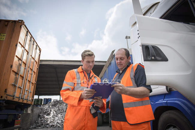 Trabajador inspeccionando el papeleo de entrega con el conductor del camión - foto de stock